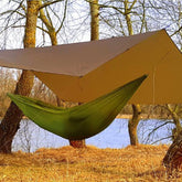 Bushmen Ultralight Tarp in Dark Olive color set up over a green hammock by a tranquil riverbank.